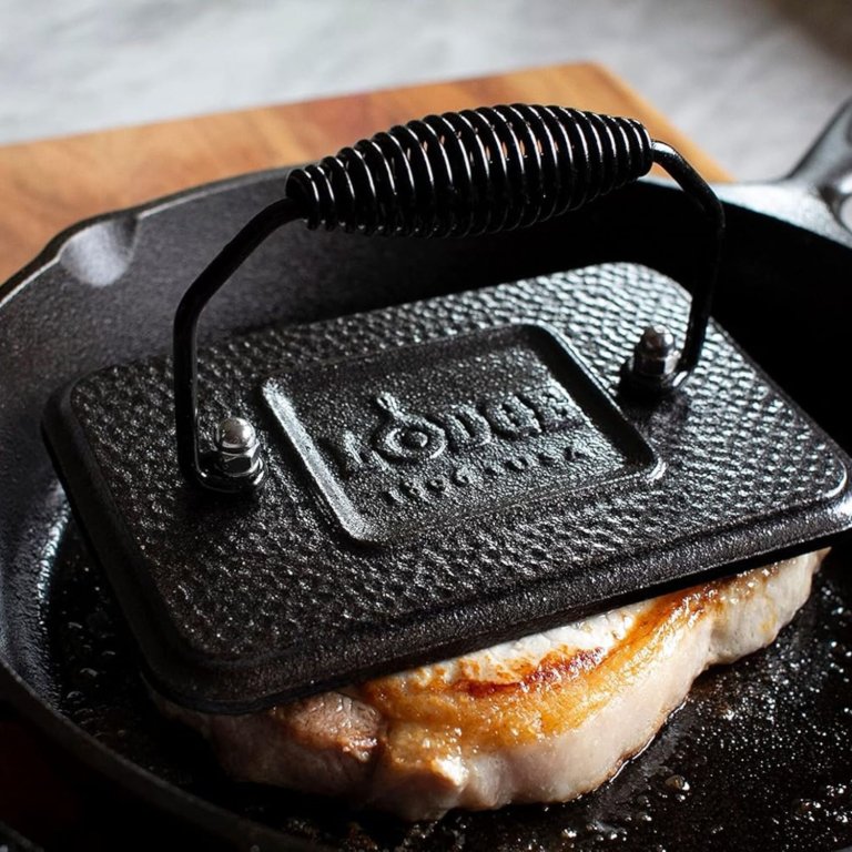 The Lodge Pre-Seasoned Cast-Iron Grill Press pressing down a piece of meat while cooking
