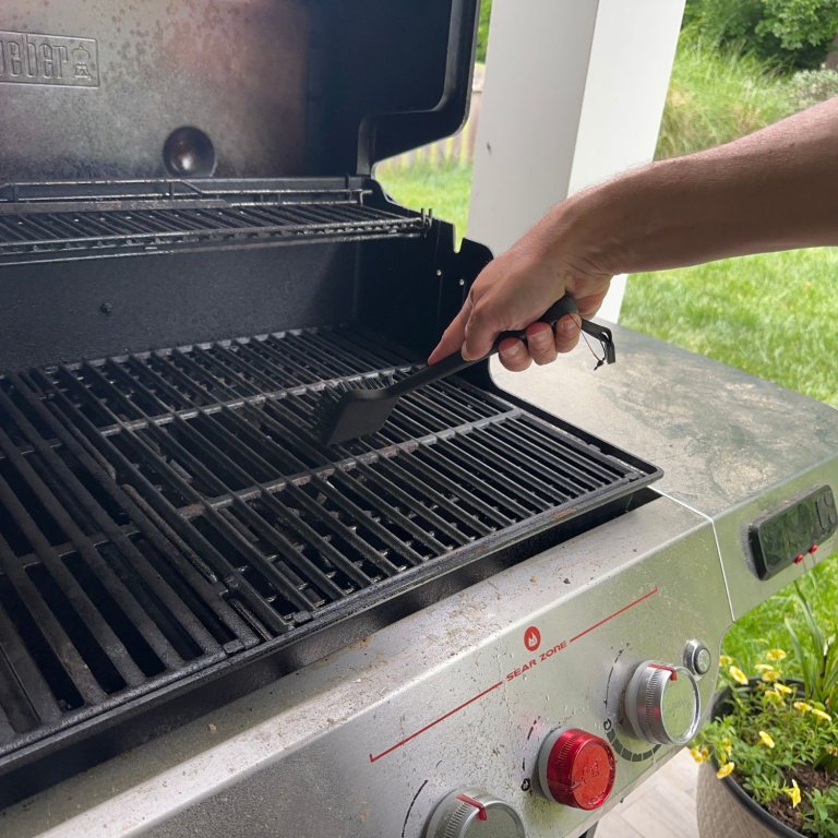 A product tester using the Ninja Woodfire Outdoor Grill Cleaning Brush to clean grill grates