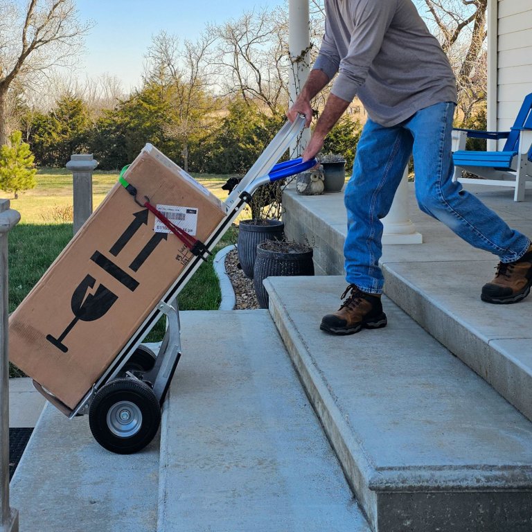 The Strongway Continuous Handle Aluminum Hand Truck being used to move a large box up stairs during testing