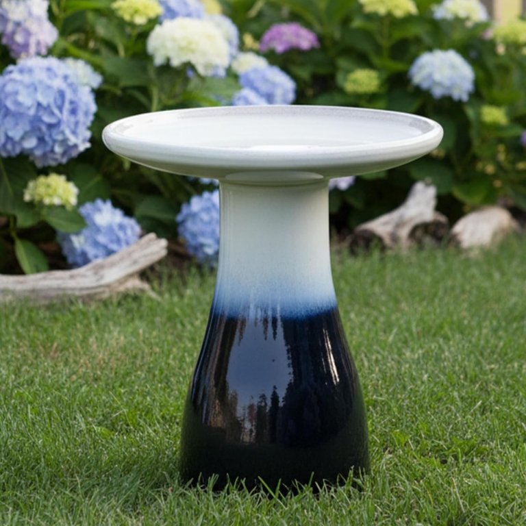 The Sunnydaze Glazed Ceramic Classic Outdoor Bird Bath in a yard with flowers