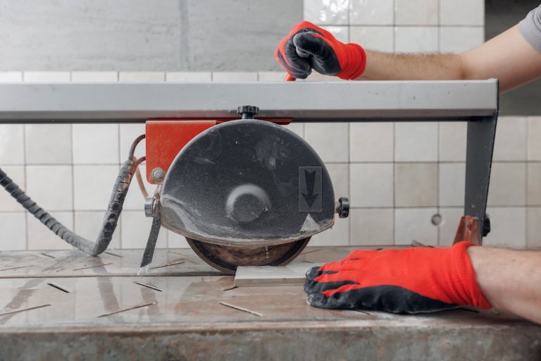 A person with work gloves uses a wet saw to cut tile as they work on a backsplash.