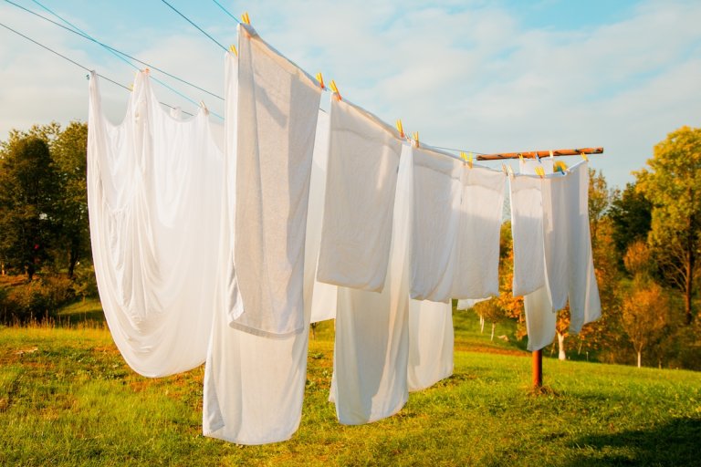 Fresh, white linens hanging from a line in a green yard.
