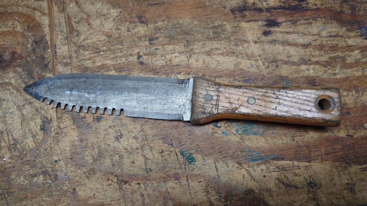 A hori-hori knife with wooden handle on top of a work bench.
