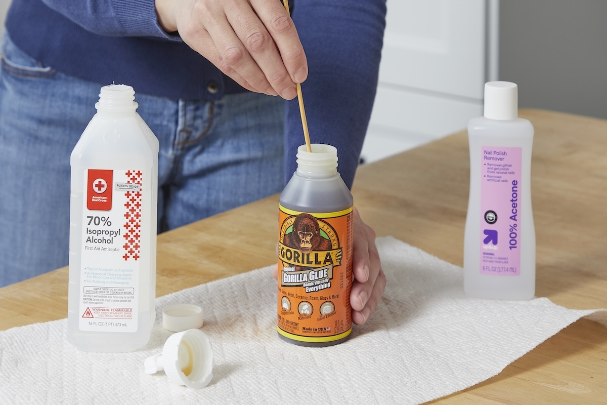 Woman stirs wood glue with a wood stirrer, bottles of isopropyl alcohol and acetone nearby.