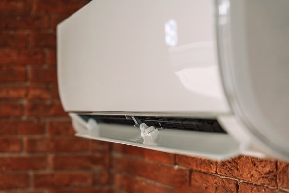 Close up view of a white mini split air conditioner on a brick wall.