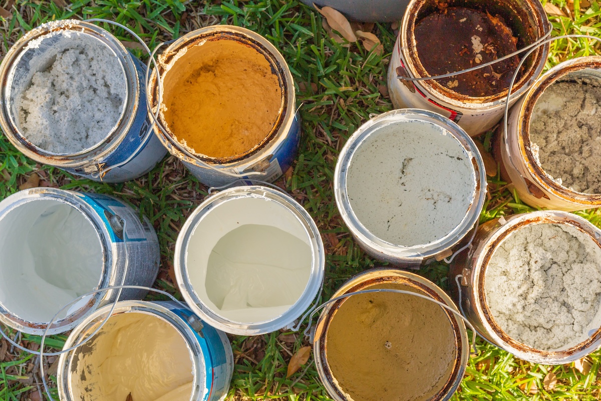 Bird's eye view of nine gallon-sized paint cans with lids off, sitting outdoors on grass.