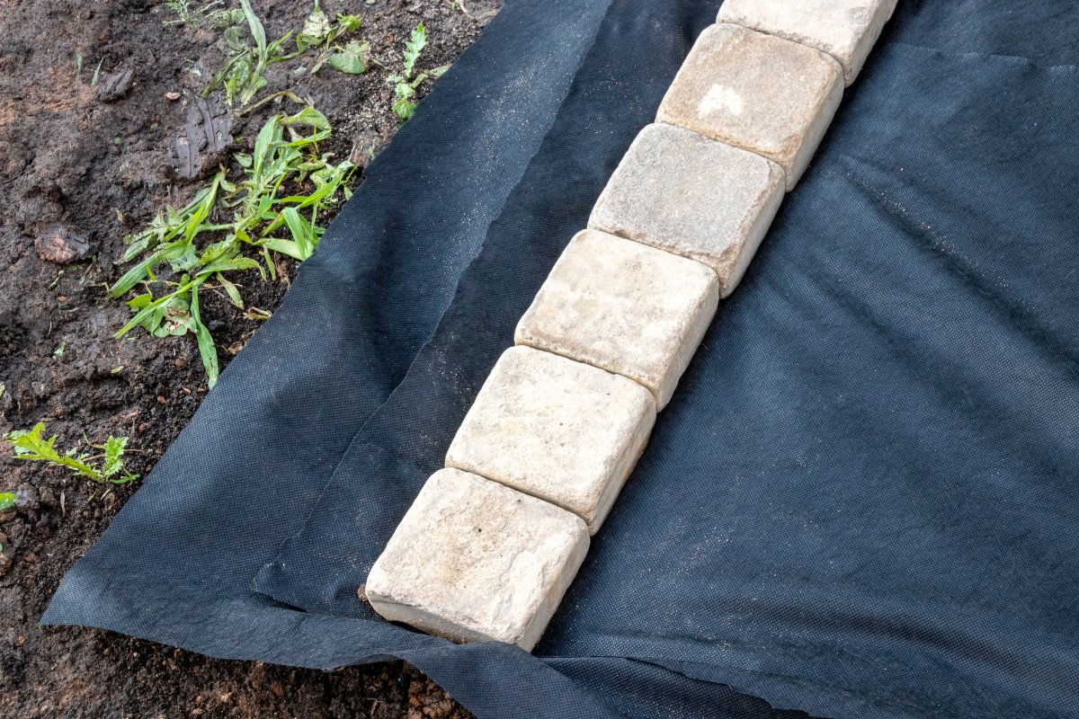 Edging of laid woven landscaping fabric with sandstone pavers in a garden. 