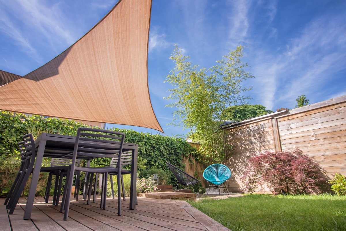 Modern house terrace in summer with table and tan shade sail.
