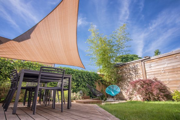 Modern house terrace in summer with table and tan shade sail.