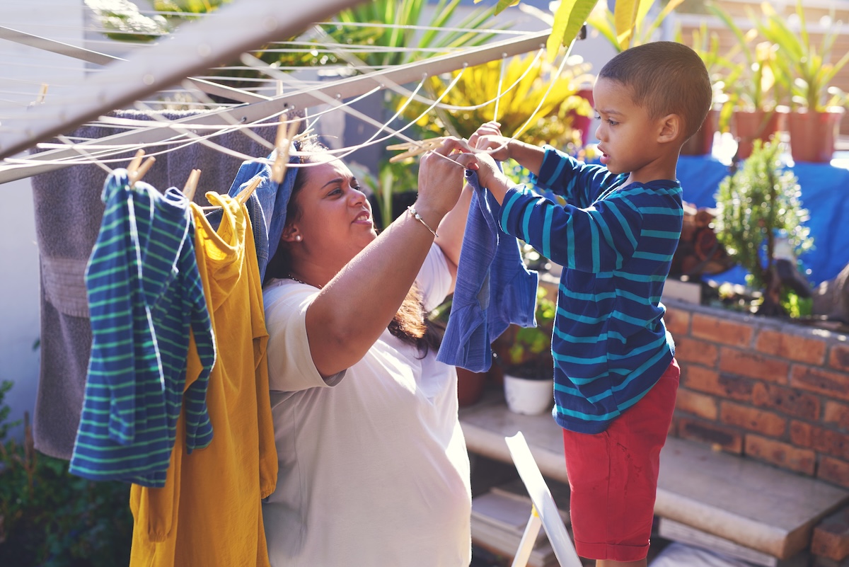 A mother and her toddler son hang colorful laundry on a clothes line.