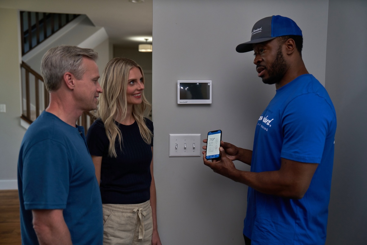 An American Standard technician installing a smart thermostat in a house.