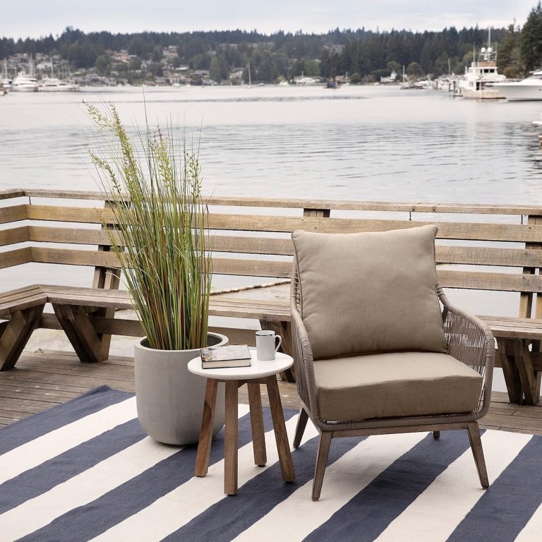 The Arden Selections Oceantex Deep Seat Cushion Set on an outdoor chair on a dock with a body of water in the background