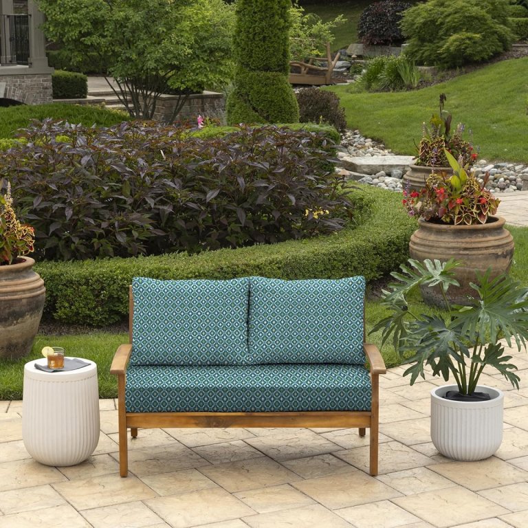 The Arden Selections Outdoor Loveseat Cushion Set on an outdoor patio surrounded by landscaping