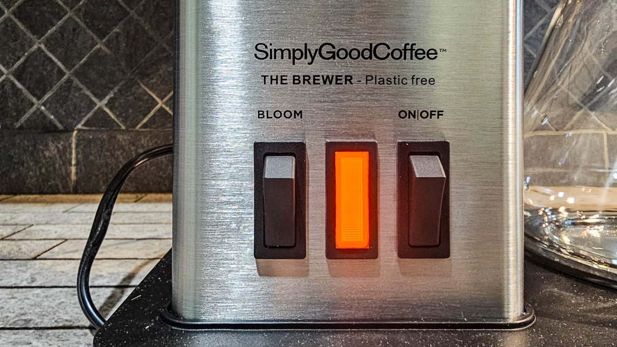 A glowing orange button on the SimplyGoodCoffee brewer showing that coffee is brewing