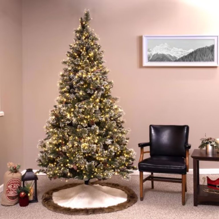 A Holiday Bright Lights Color-Changing Christmas Tree set up next to a chair and table