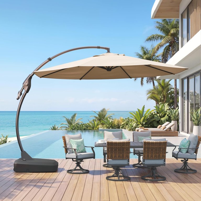 The Grand Patio Deluxe Napoli Cantilever Patio Umbrella set up over an outdoor table and chairs with a pool and the ocean in the background
