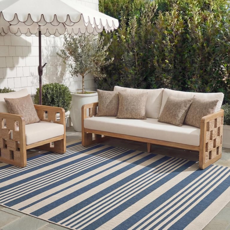 The Safavieh Courtyard Collection Indoor Outdoor Rug on an outdoor patio with a couch, chair, and patio umbrella on it