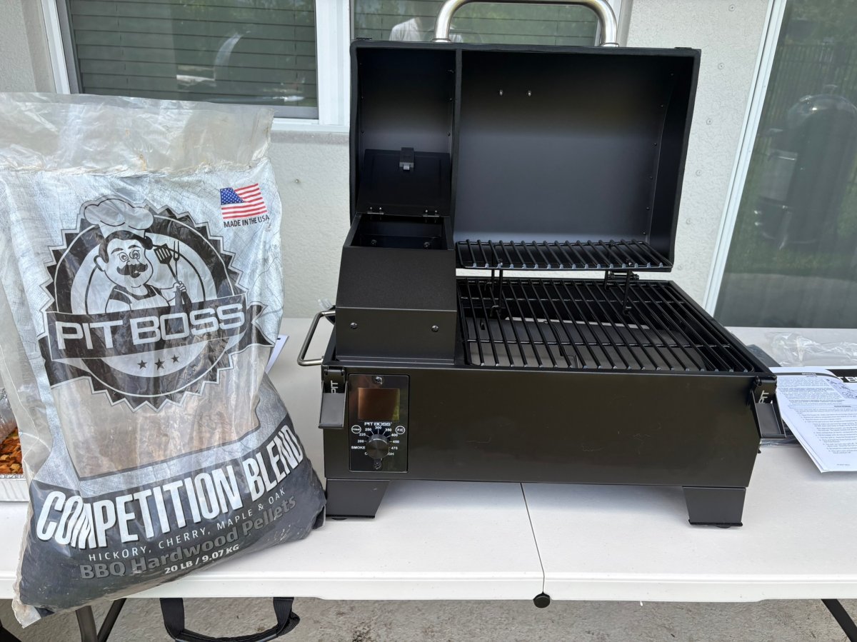 The Pit Boss Portable Tabletop Wood Pellet Grill set up outside on a table next to a bag of hardwood pellets