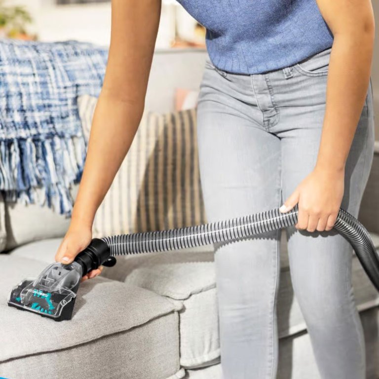 A person using an upholstery cleaner to clean a cream couch cushion