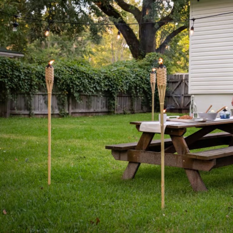 Two TIKI Bamboo Outdoor Torches set up next to an outdoor picnic table