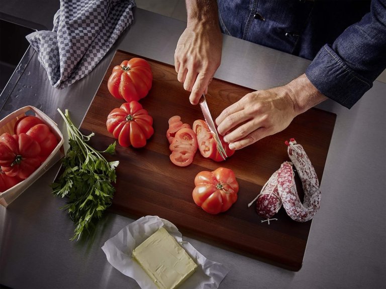 A dad using the üsthof Classic 2-Piece Chef's Knife Set to cut tomatoes and sausage