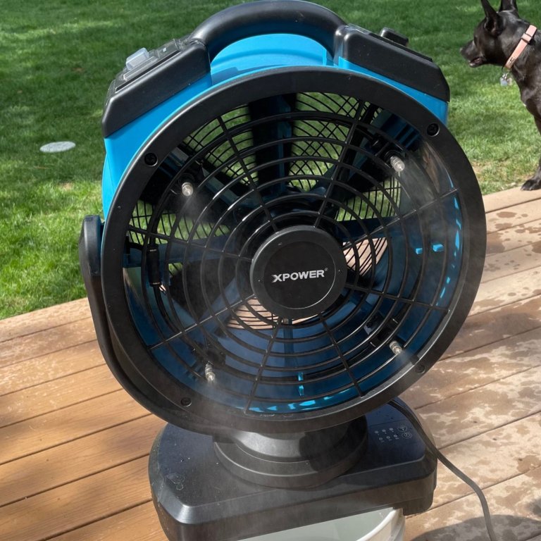 The XPower FM-88W Oscillating Misting Fan With Water Pump on a 5-gallon bucket blowing a cool mist across a deck