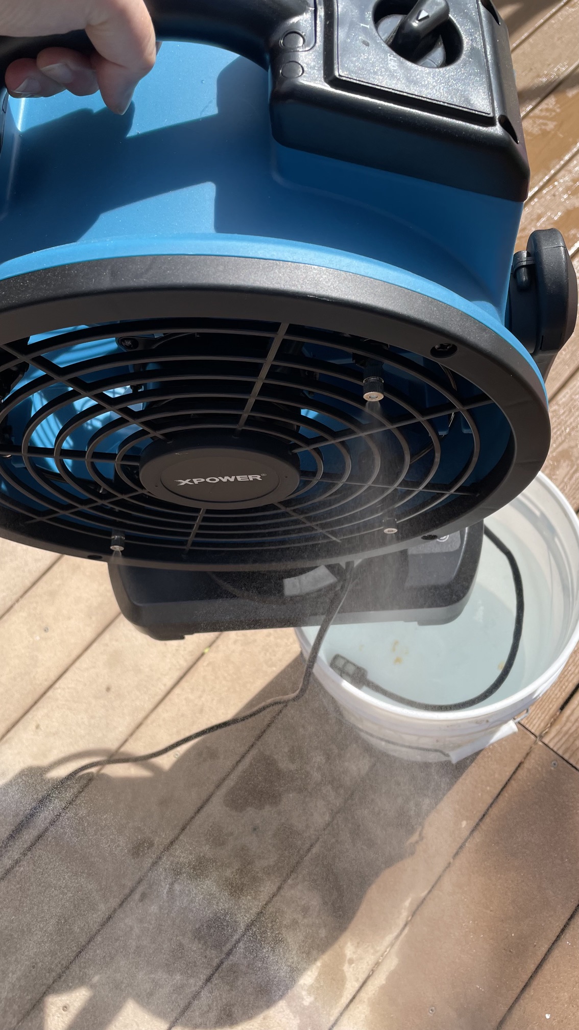 A person holding the XPower FM-88W misting fan by its handle to show the water pump in a bucket of water