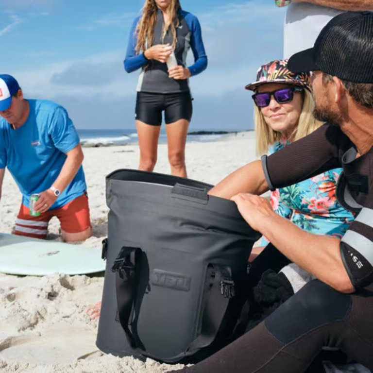 A group on a beach with one member reaching into a Yeti Hopper Soft-Sided Cooler