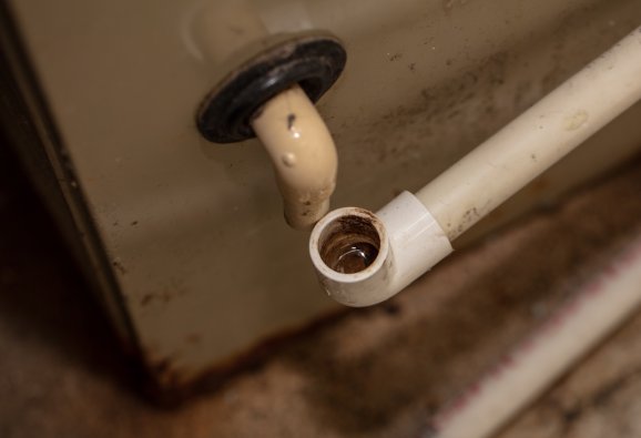 The drain pipes of an air conditioner with grime and build-up that needs cleaning.