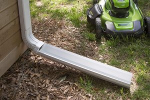A retractable downspout extender next to a lawn mower.