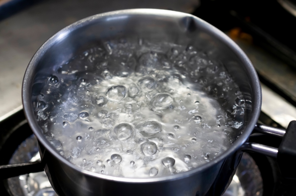 Steel pot of boiling water on a stove burner.