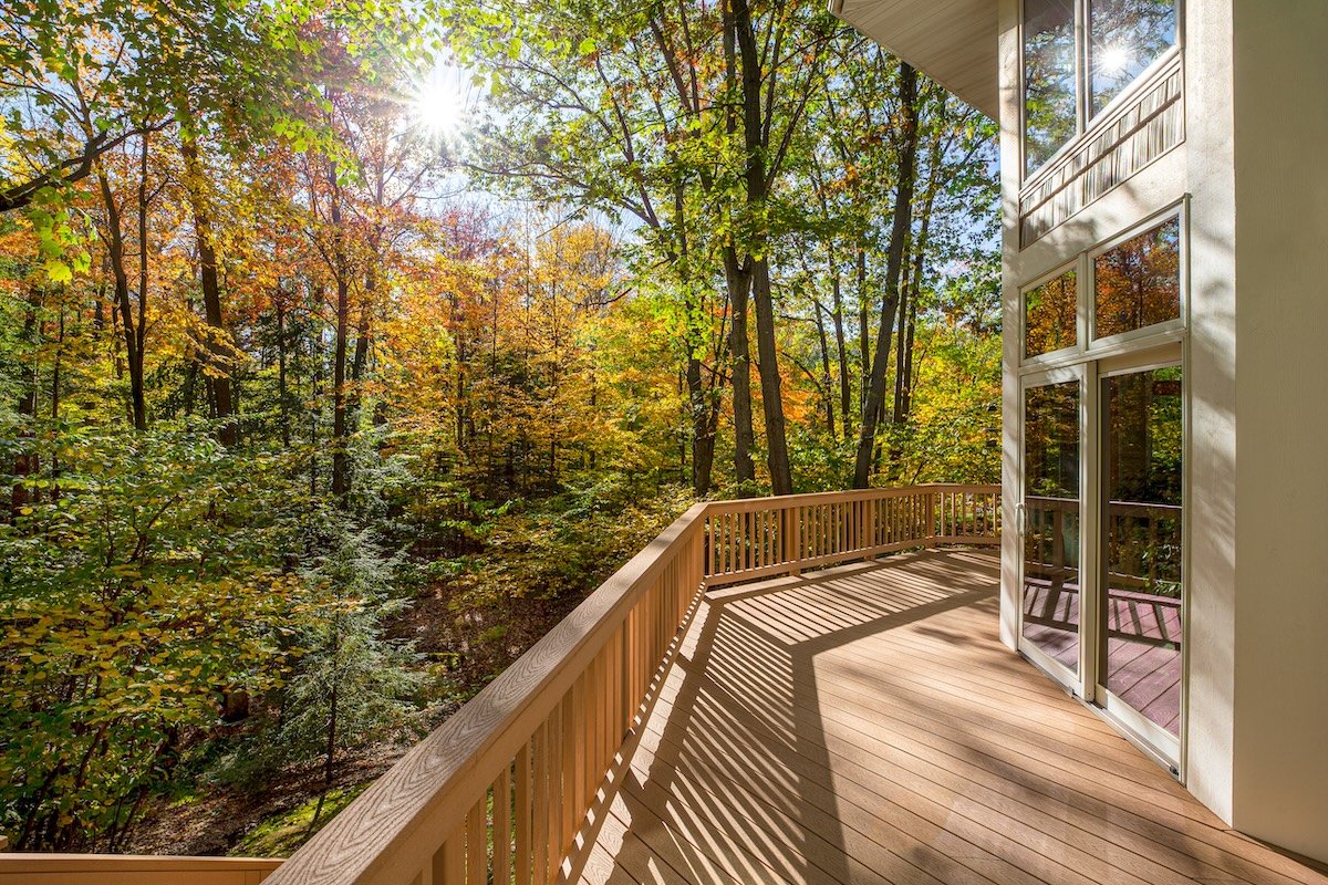 View from the deck of a luxury home in the autumn woods. Outdoor living concept, bright fall foliage, and intentional sun flare highlight.