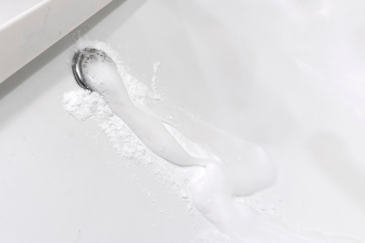Foamy mixture of baking soda and vinegar oozes from a bathroom sink overflow hole.