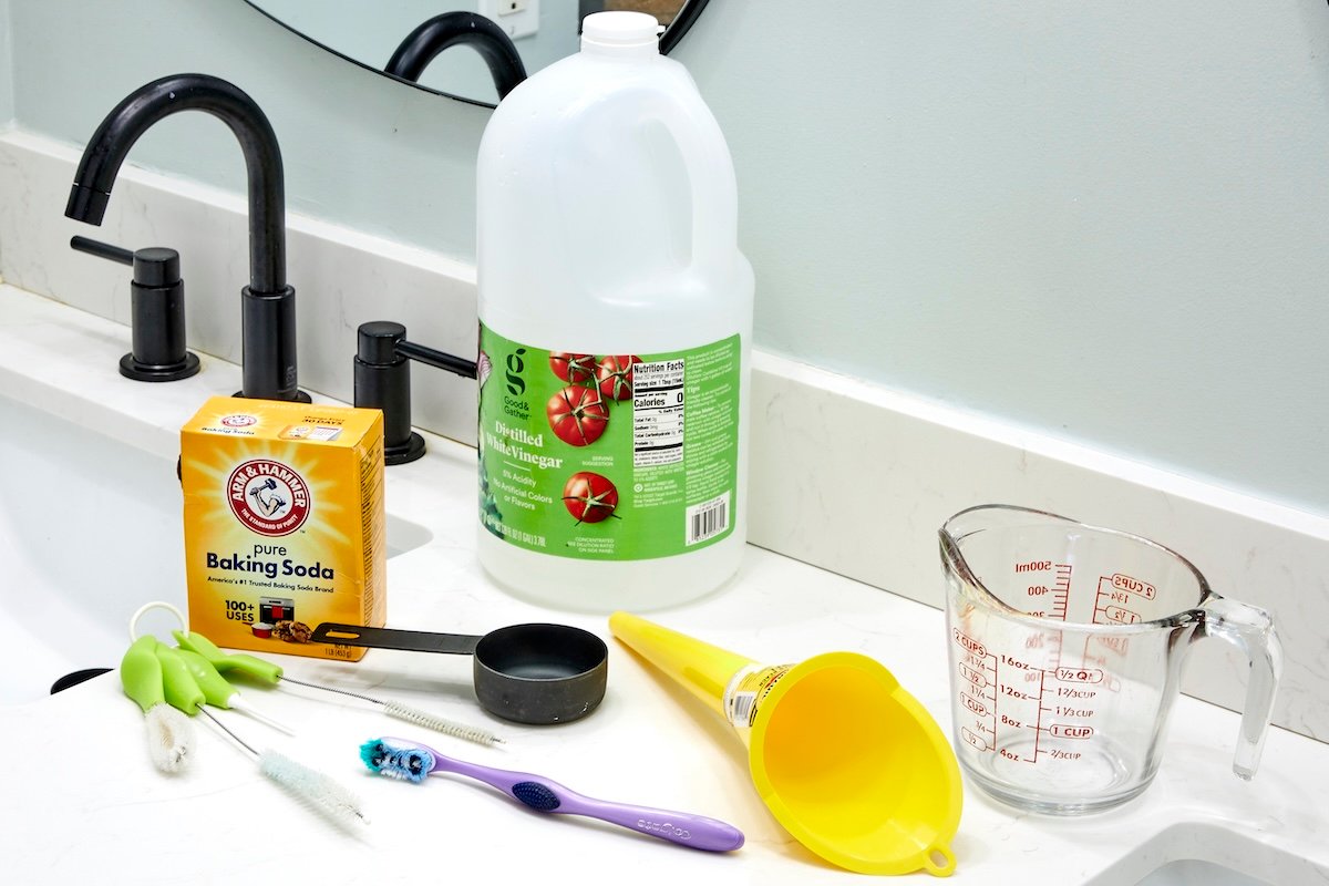 Vinegar, baking soda, funnel, measuring cup and scrub brushes on top of a sink vanity.