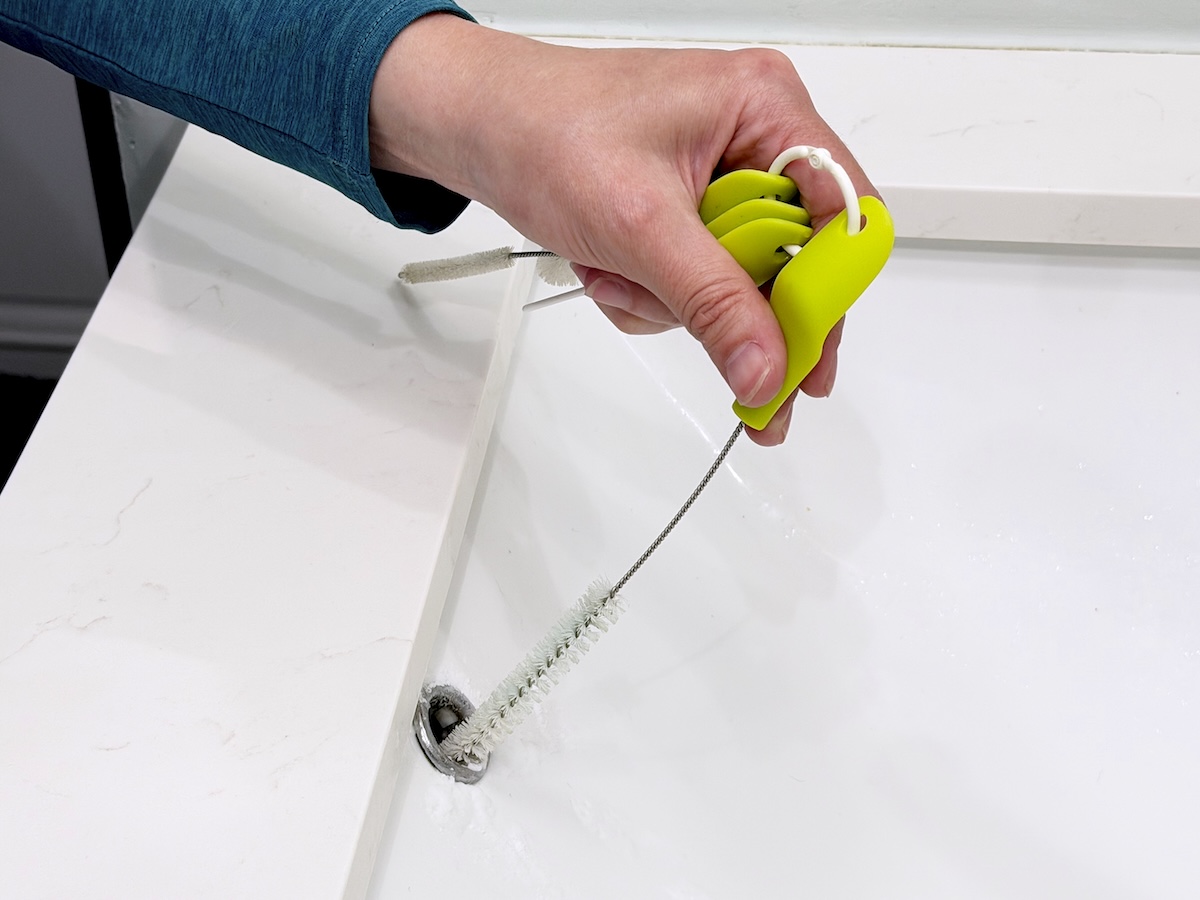 Woman inserts narrow scrub brush into the hole in the front of a bathroom sink.