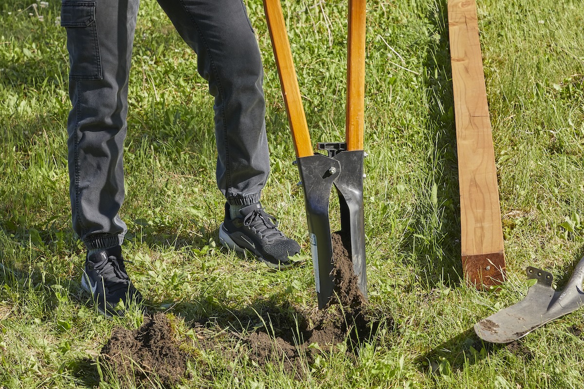 Woman pulls a manual post hole digger clamping soil out of the ground.