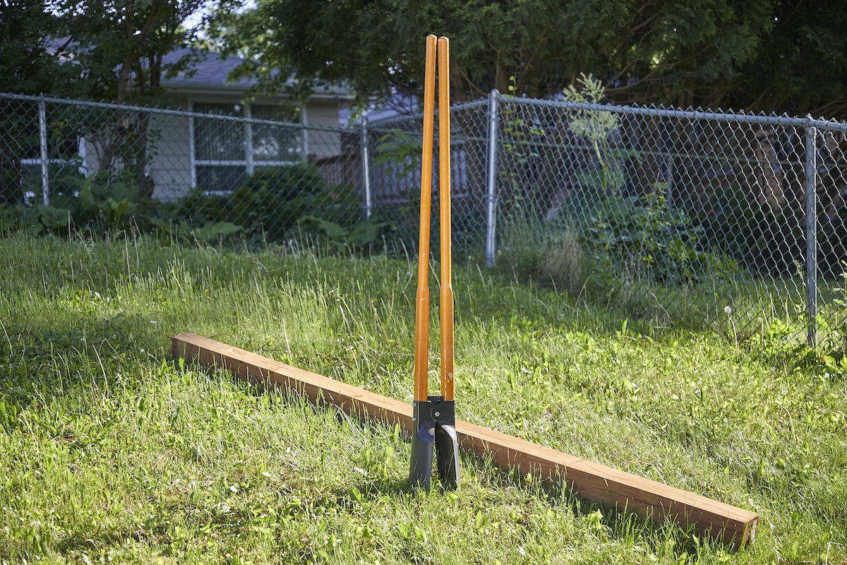 Post hole digger standing vertically in the ground with a post laying on the ground behind it.