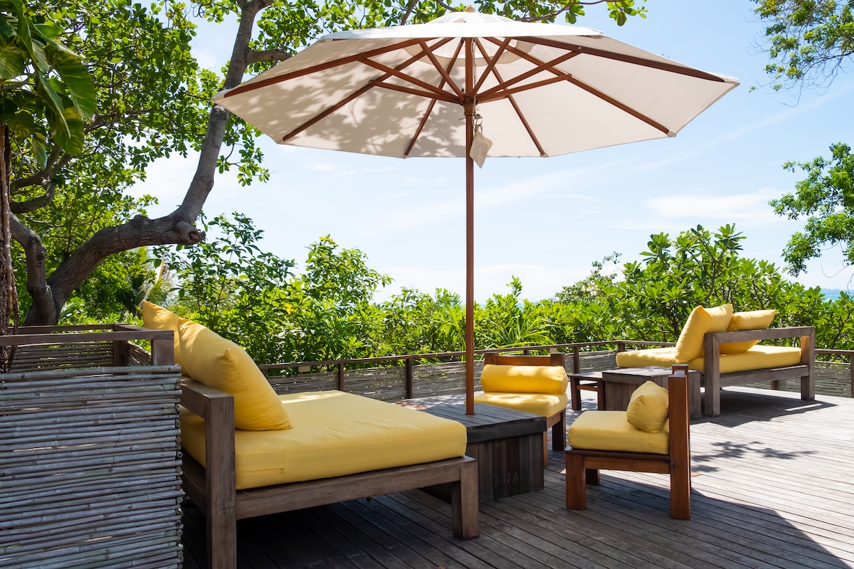 Large umbrella open over patio furniture with yellow cushions, on a wood deck.