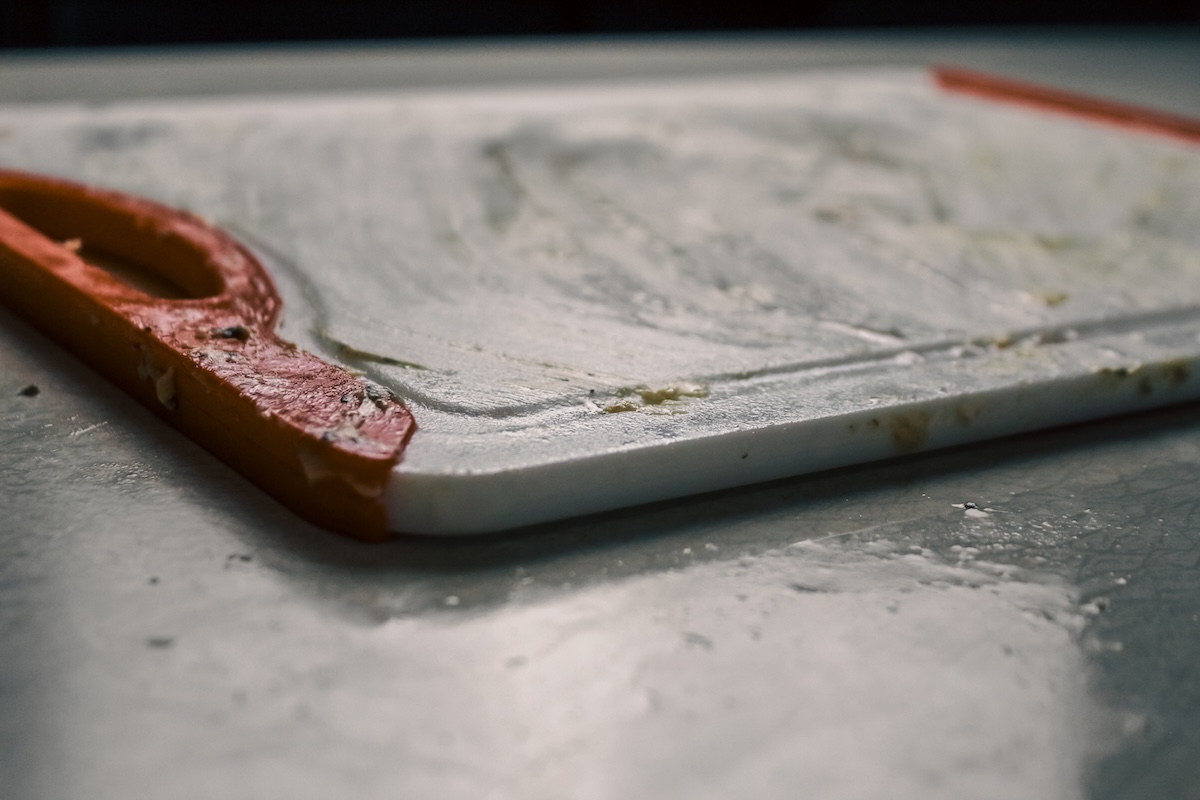 Close-up of a used plastic cutting board with food debris and juices in need of cleaning. Food safety design element or background.
