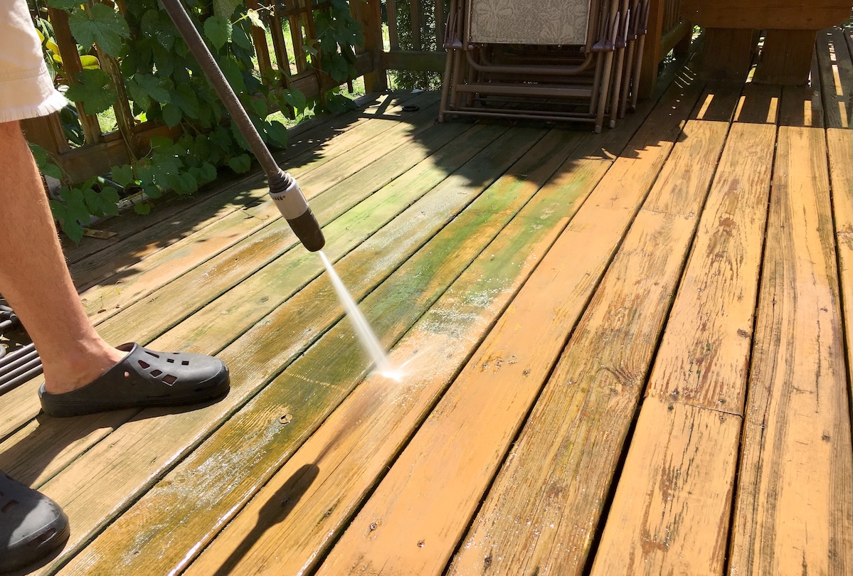 Man wearing Crocs pressure washing a mildewy deck.
