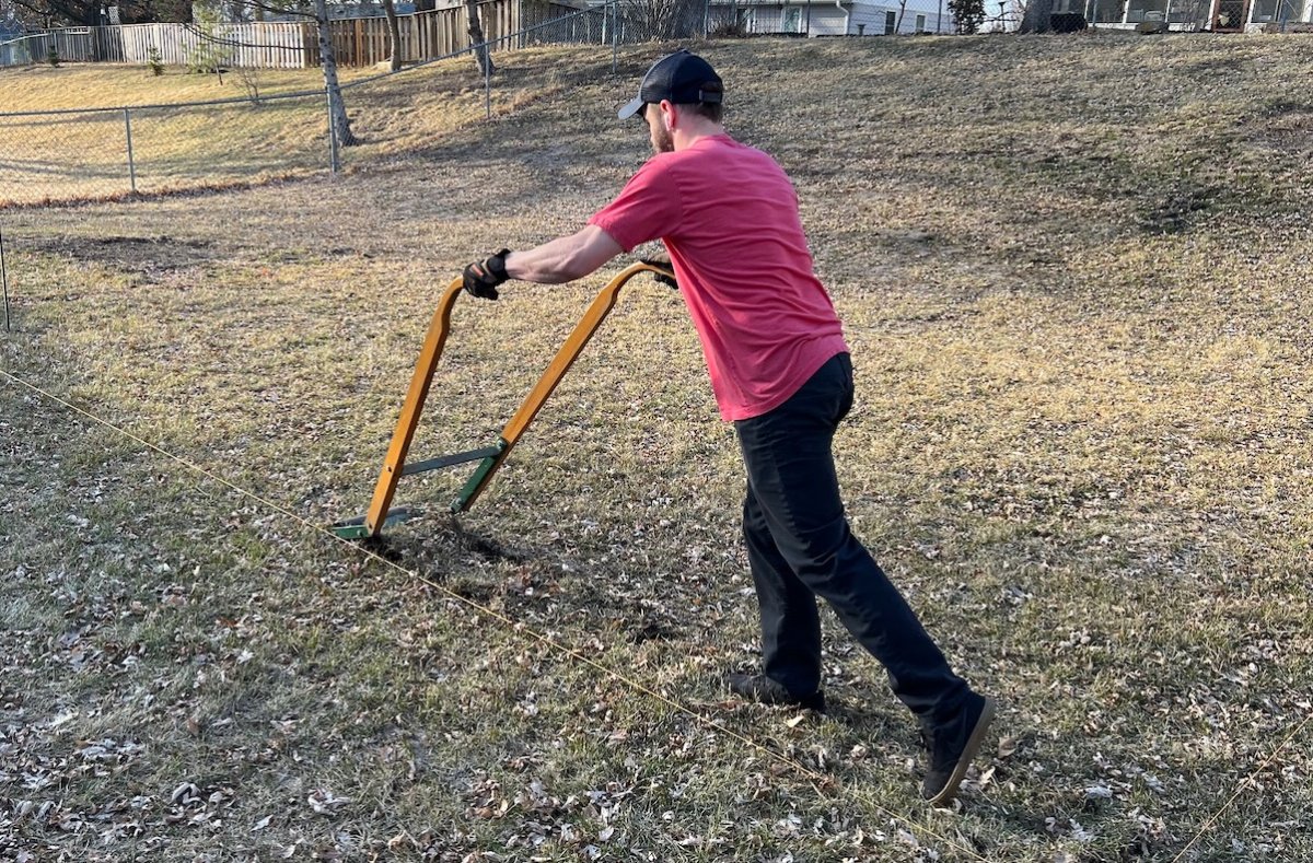 Man in red shirt and ball cap pushes a sod cutter.