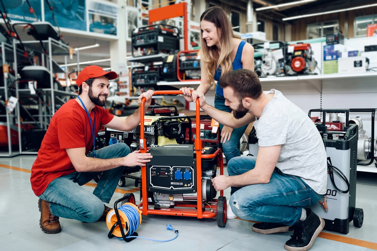 A young couple discusses a portable generator with a salesperson in a hardware store.