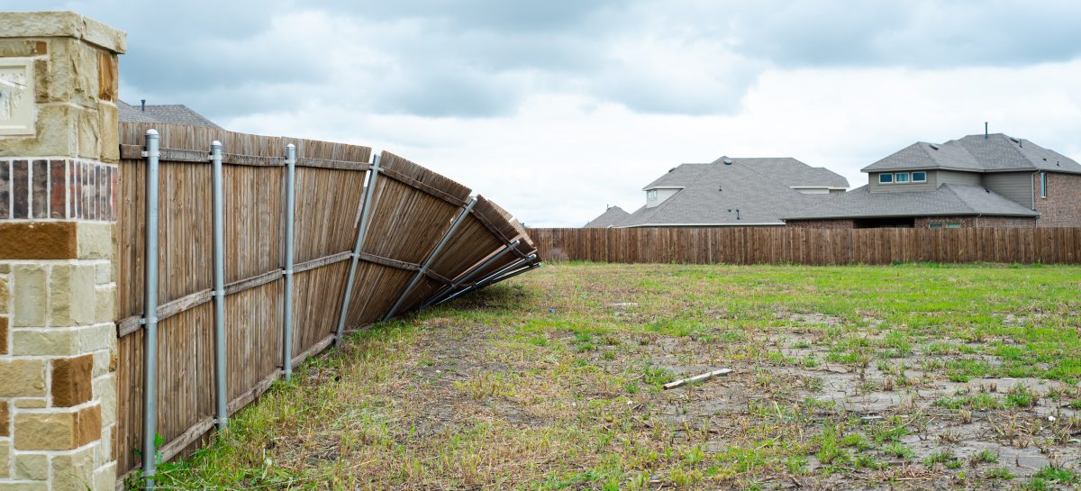 Collapsed wooden fence with neighborhood homes in background