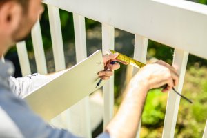 Man with a white hard hat holding a clipboard, measuring deck fence