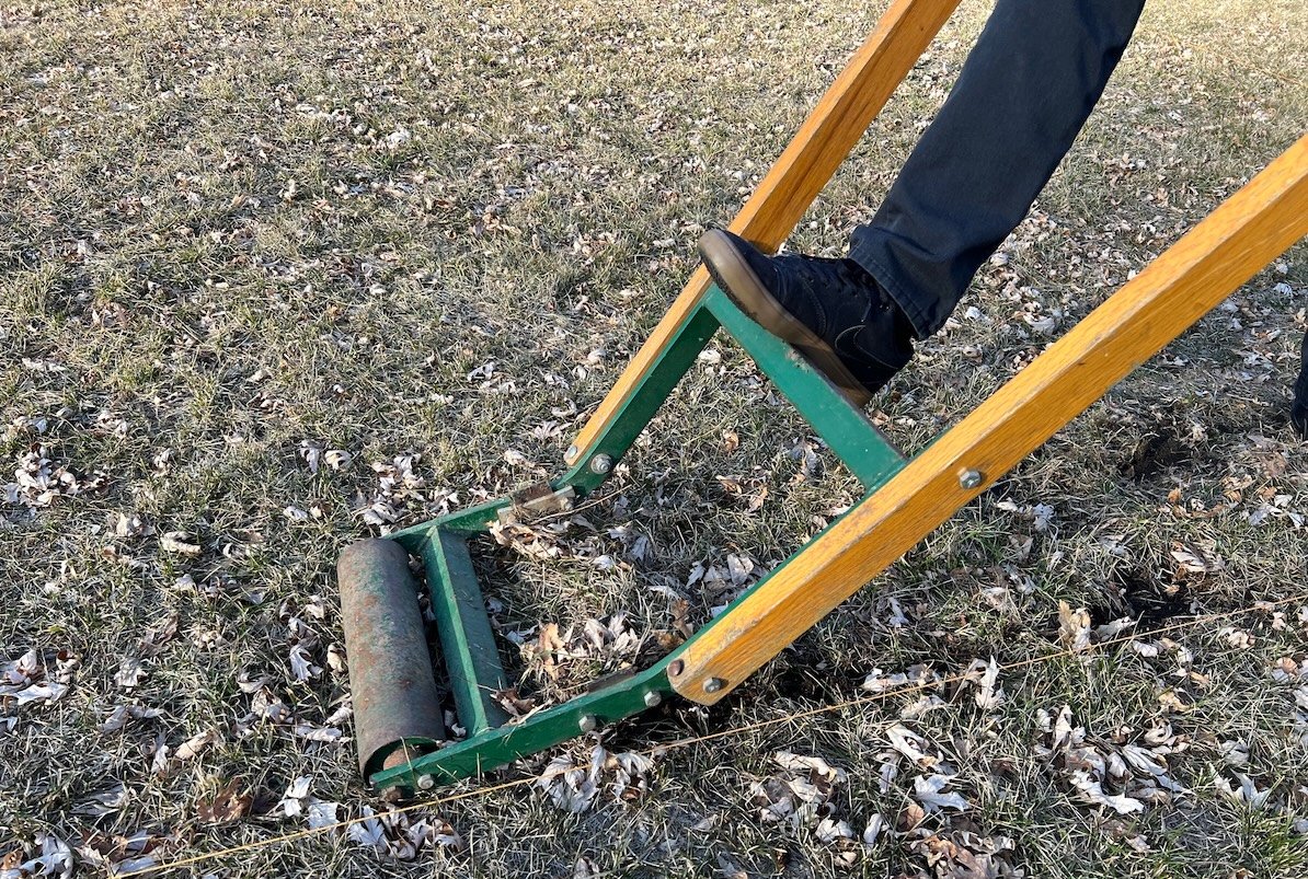 Man with his foot on top of a manual sod kicker, preparing to kick it.