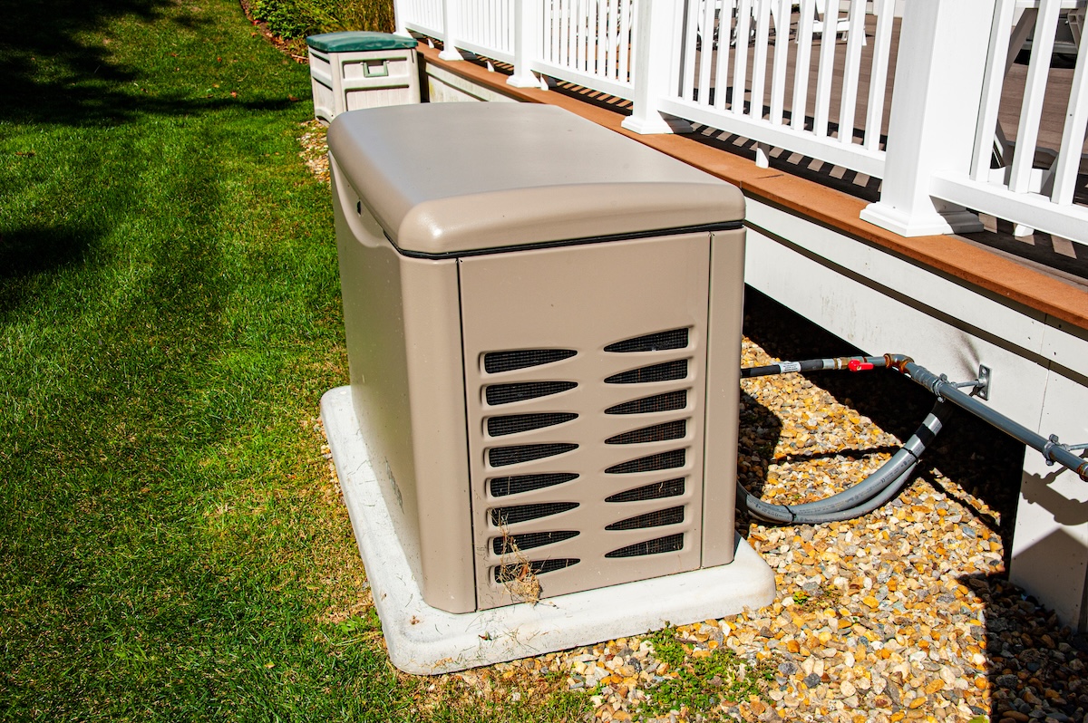 A midsized standby generator next to the deck of a modern home.