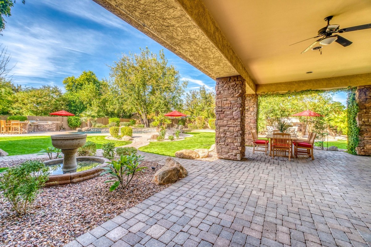 Large stone patio of a luxury house shaded by a roof overhang, with gravel garden beds adjoining.