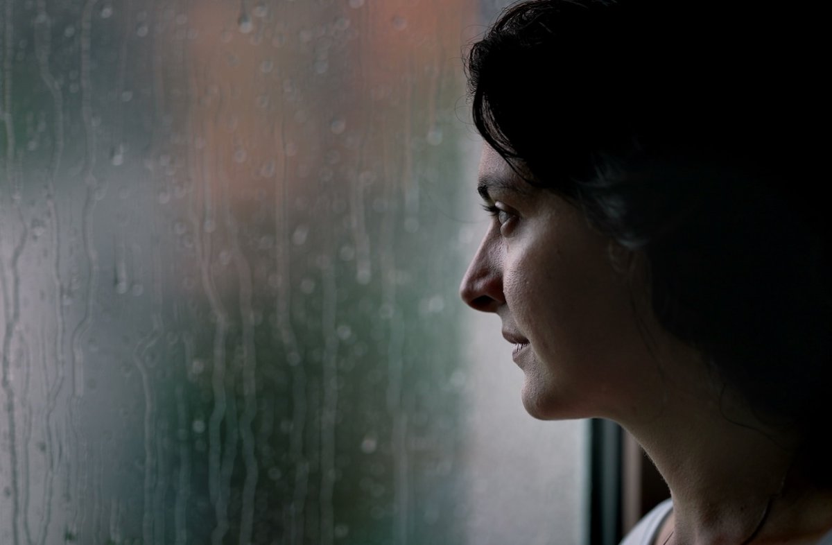 Woman standing by window looking outside watching rain.