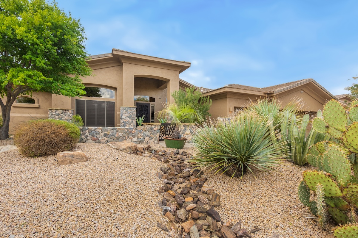 Front of a stucco home landscaped with gravel, a stone path, and drought-tolerant plants.