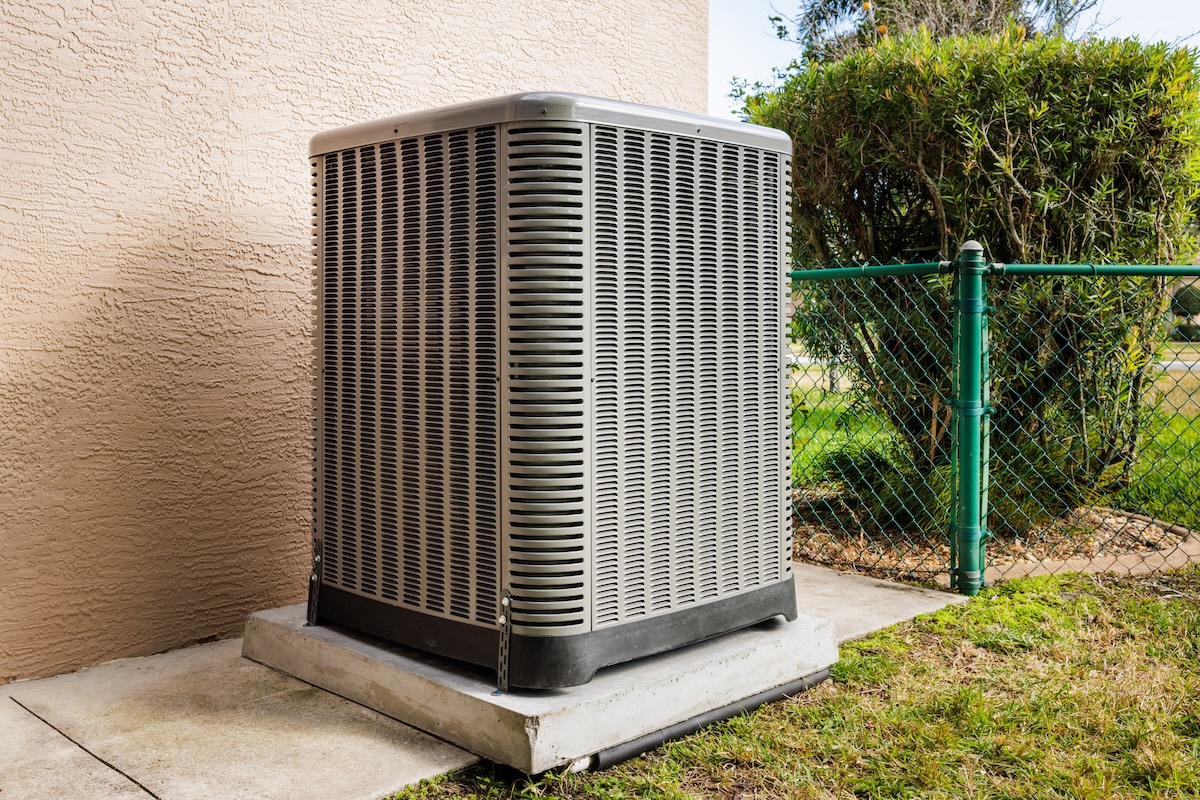 Metal air conditioning unit outside a house, on a concrete slab.